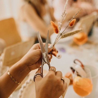 Hände, die Draht für einen kleinen Trockenblumenstrauß für den Makramee Kranz abschneiden